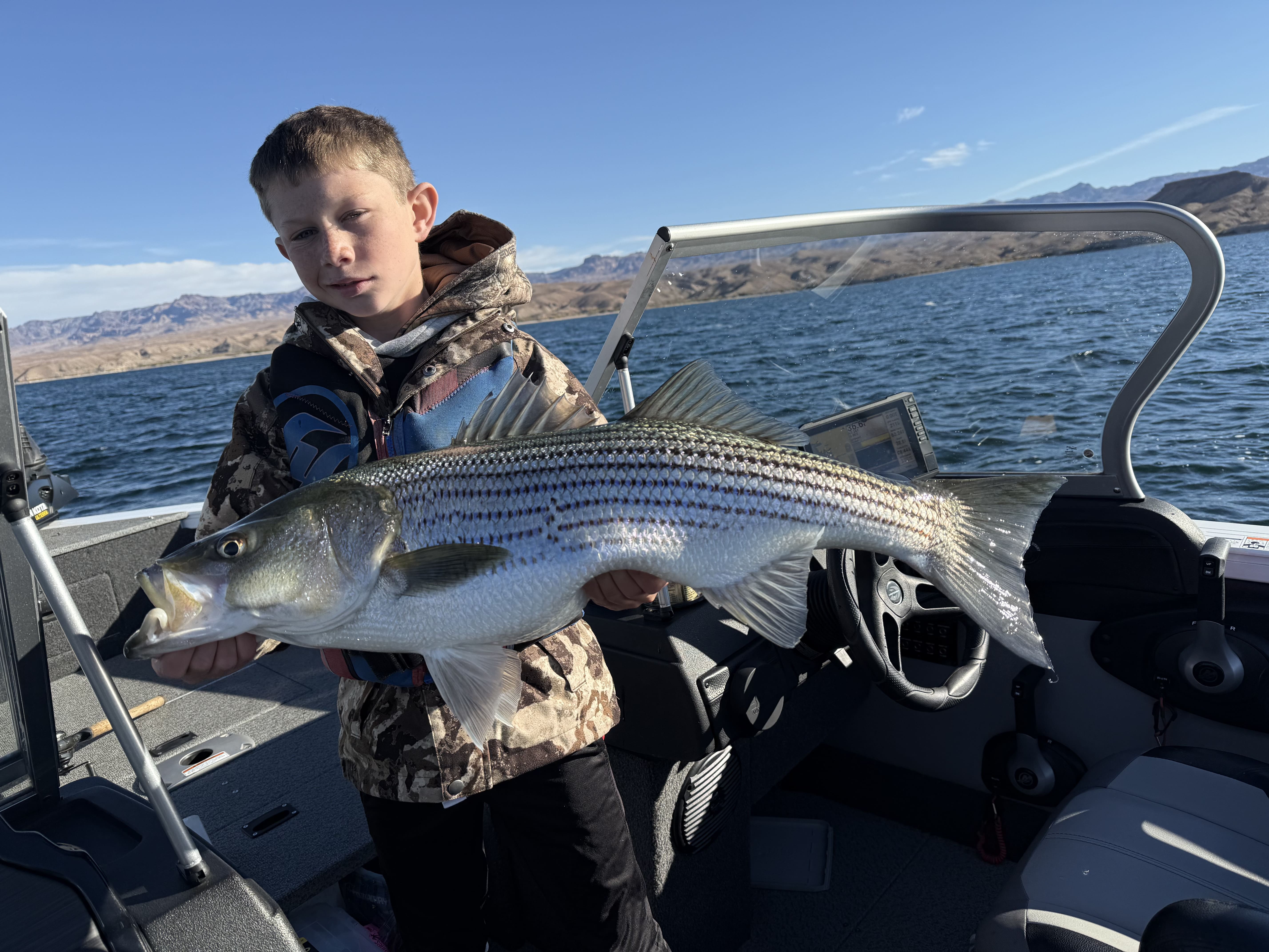 Youth angler holding a large striped bass on the boat