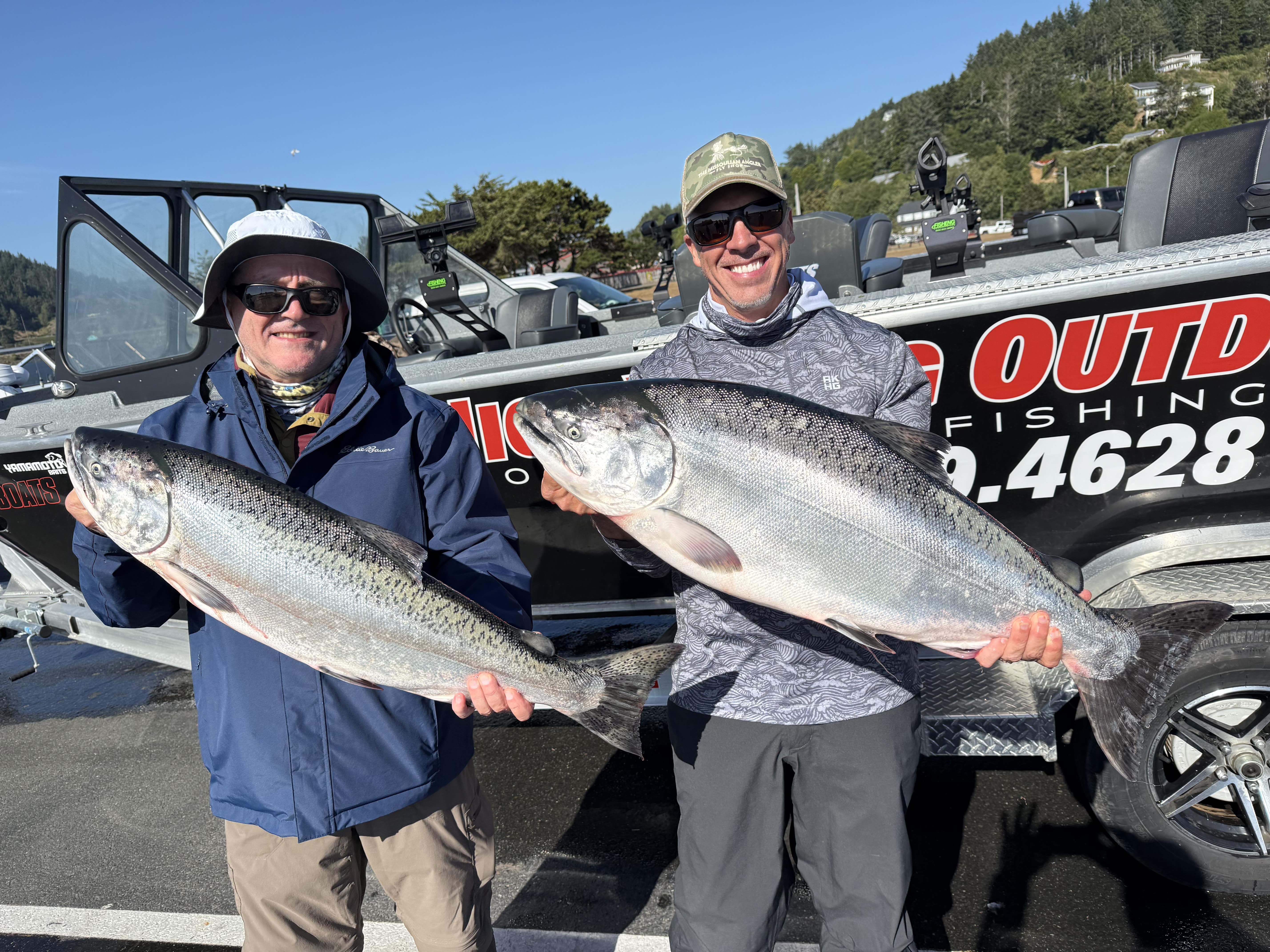 Two anglers each holding a Chinook salmon in front of the boat