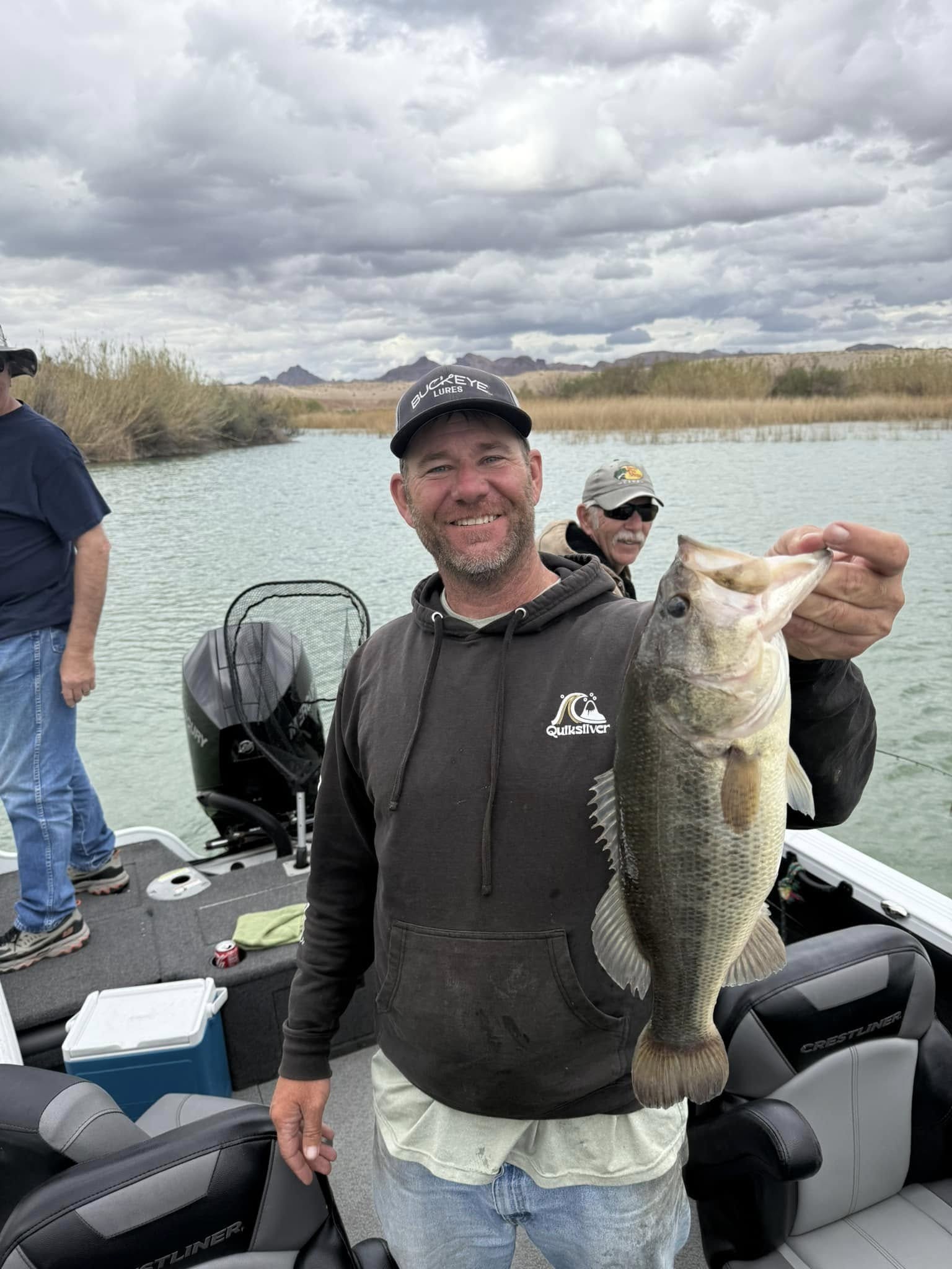 Angler holding a largemouth bass with reeds and mesas in the background